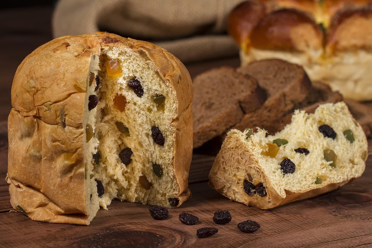 Angeschnittener Hefekuchen mit Rosinen auf einem Holzbrett, daneben einzelne Rosinen
